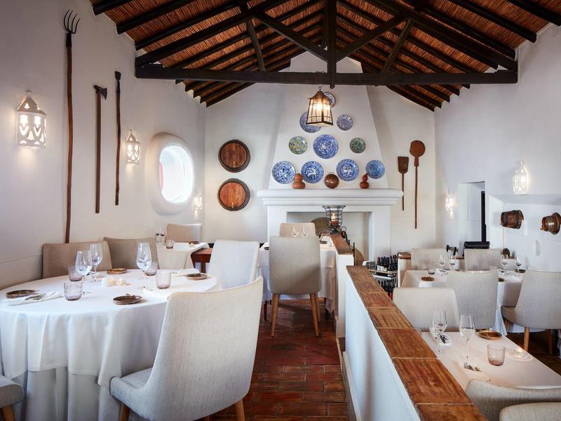 Elegantes Restaurant mit weißen Tischen, bequemen Stühlen und Holzbalkendecke, dekorative Teller an der Wand.