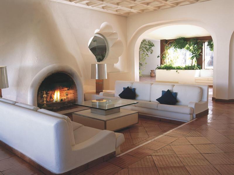 Gemütliches Wohnzimmer mit weißem Sofa, offenem Kamin, großen Fenstern und Holzdecke.