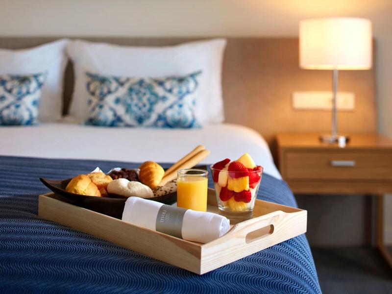 Ein Tablett mit Frühstück auf blauem Bett, im Hintergrund Nachttisch mit Lampe und Kissen.