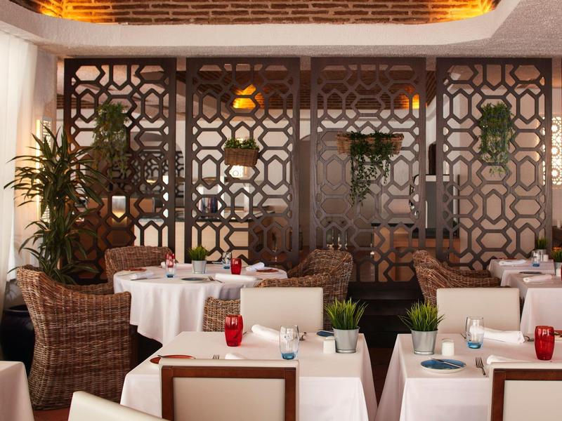 Elegantes Restaurant mit weißen Tischtüchern, Korbstühlen und dekorativen Wandelementen.