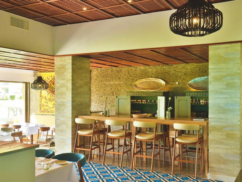 Innenraum eines Restaurants mit Holzmöbeln, gemustertem blauen Teppich und natürlichem Licht.