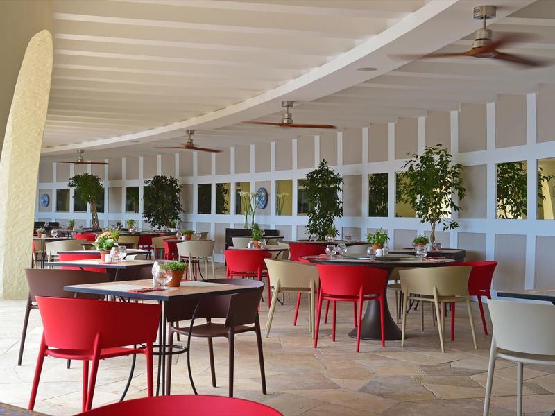 Großer, offener Restaurantbereich mit weißen Wänden, roten und grauen Stühlen und grünen Pflanzen.