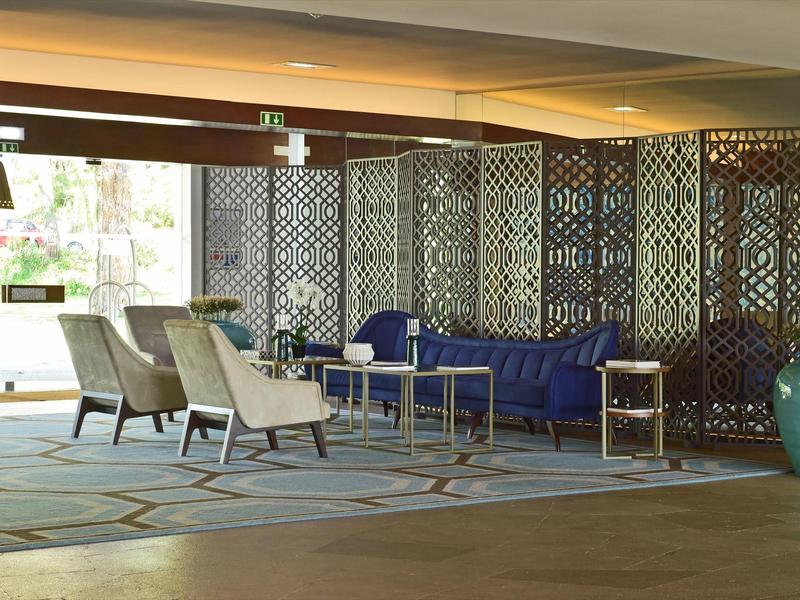 Moderner Aufenthaltsraum mit blauen Sofas, beigen Sesseln, Teppich und dekorativen Raumteilern.