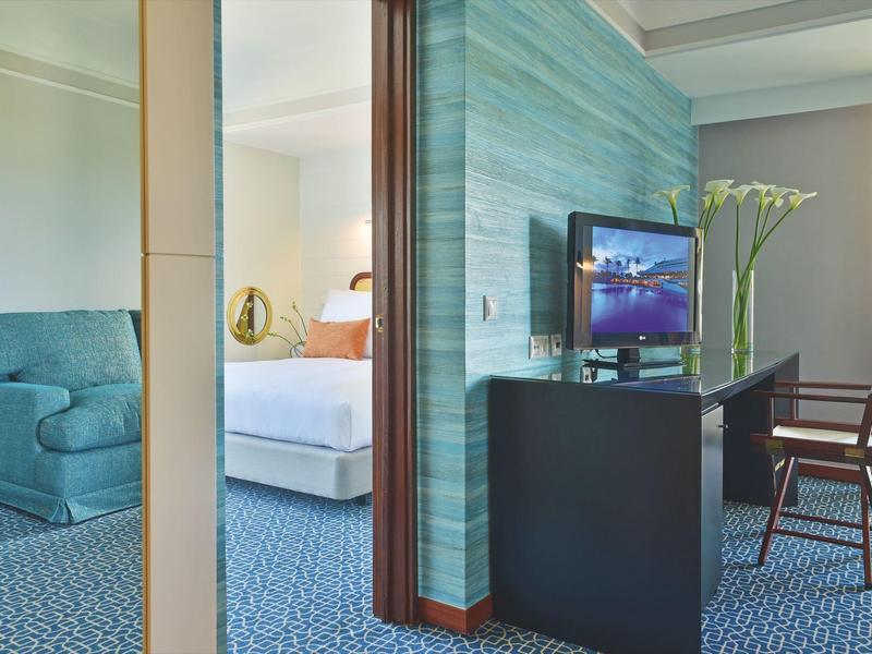 Elegantes Hotelzimmer mit blauem Teppich, grün gestreifter Wand und moderner Einrichtung.