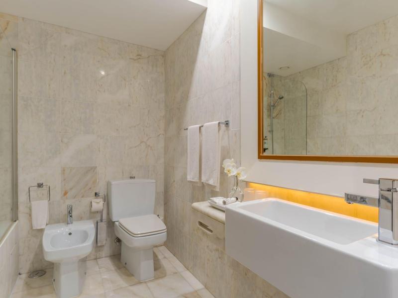 Modernes Badezimmer mit weißem WC, Bidet, eckigem Waschbecken und großem Spiegel an Marmorwänden.