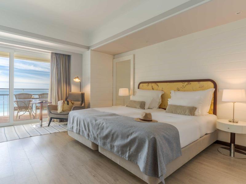 Helles Schlafzimmer mit großem Bett, zwei Nachttischen, Sesseln und Balkon mit Meerblick.