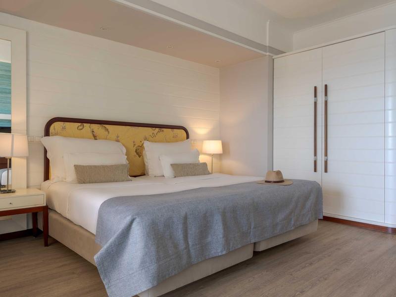 Modernes Schlafzimmer mit großem Bett, grauer Decke, zwei Nachttischen und weißem Kleiderschrank.