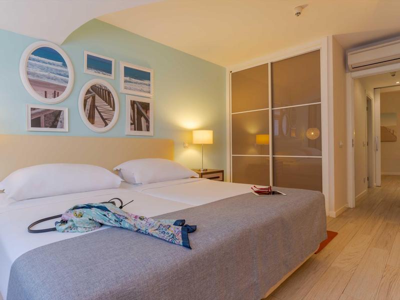 Modernes Schlafzimmer mit großem Bett, hellen Holzböden, Wandkunst und Kleiderschrank aus Glas.