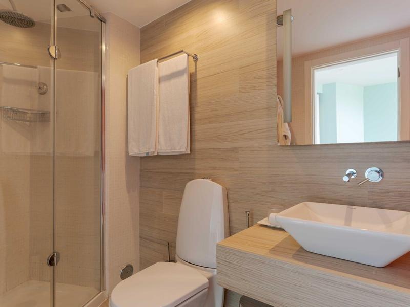 Modernes Badezimmer mit Glas dusche, weißer Toilette, Waschtisch und Wandfliesen in Beige.