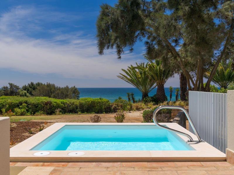 Kleiner Pool mit türkisfarbenem Wasser, umgeben von Terrasse, Palmen und Blick auf das Meer.