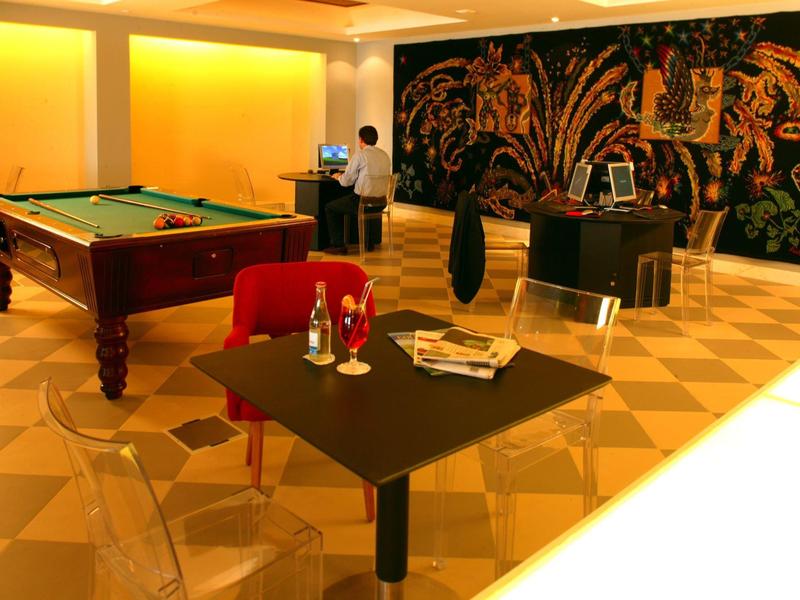 Innenraum mit Billardtisch, Schachspiel, roten Sesseln, transparenten Stühlen und großer bunter Wandkunst.