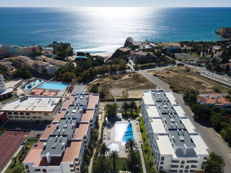 Luftaufnahme von Gebäuden und Pool mit Meer im Hintergrund bei Sonnenlicht.