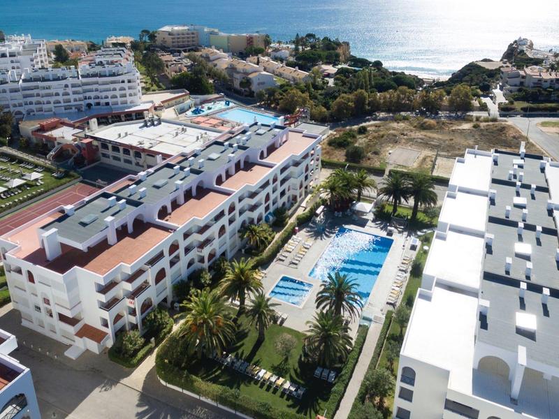 Luftaufnahme eines Hotels mit Pool, Garten und umliegenden Wohngebäuden am Meer.