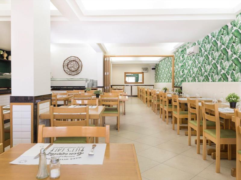 Heller, moderner Speiseraum mit Holzmöbeln, grüner Wandgestaltung und viel Tageslicht.