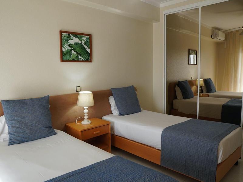 Zwei Einzelbetten mit blauen Kissen und Decken, Nachttisch und Spiegel im Hotelzimmer.