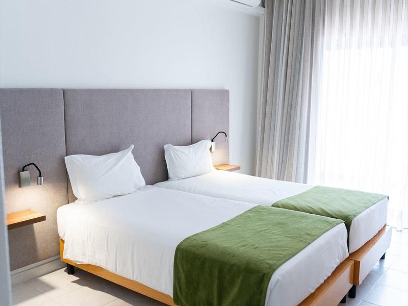 Modernes Hotelzimmer mit zwei Einzelbetten, grauem Kopfteil und grünen Decken.