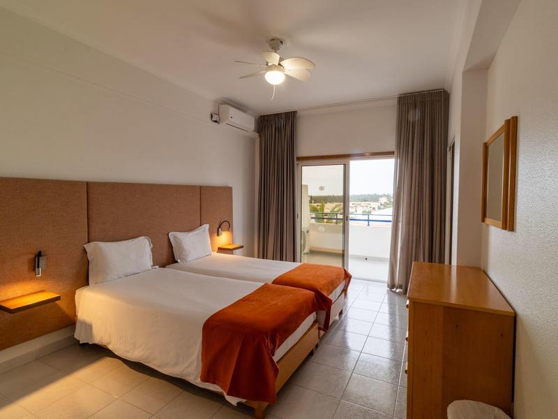 Hell eingerichtetes Hotelzimmer mit Doppelbett und Balkon mit Meerblick.