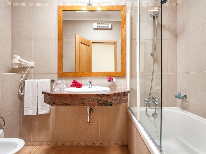 Hell gefliestes Badezimmer mit Badewanne, Wandspiegel, Holzrahmen und Waschtisch mit Marmorplatte.