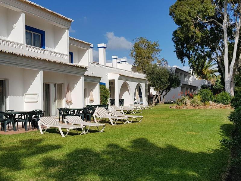 Moderne weiße Häuser mit blauen Fenstern, großen Terrassen und grünem Garten bei Sonnenschein.