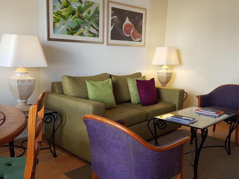 Gemütliches Wohnzimmer mit grünem Sofa, violetten Sesseln, Holztisch und zwei Tischlampen.