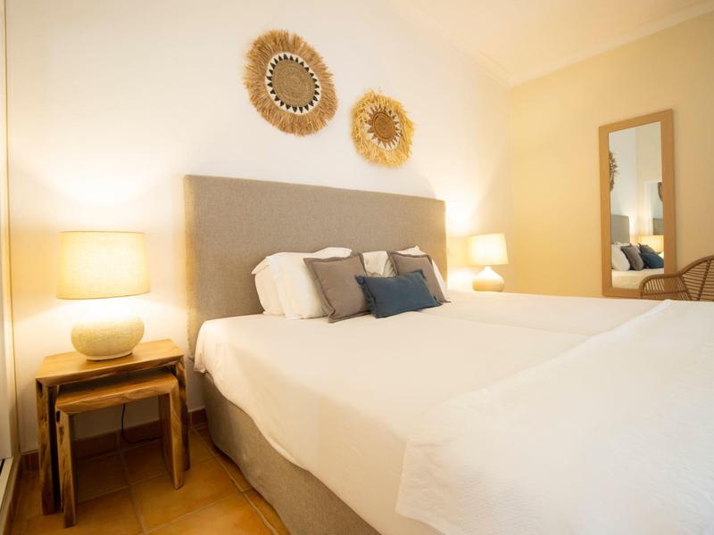 Helles Schlafzimmer mit großem Bett, zwei Nachttischen, Lampen und dekorativen Wandspiegeln.