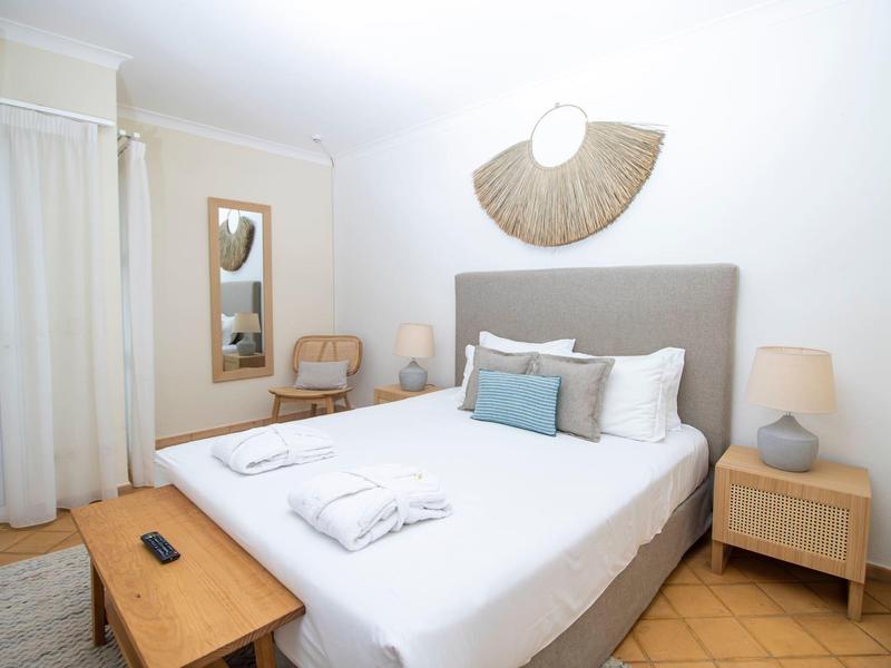 Helles Schlafzimmer mit grauem Bett, Holzmöbeln, weißen Wänden und dekorativem Wandlicht.