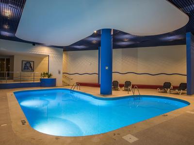 Innenpool mit geschwungener Form, blauer Beleuchtung, Säulen und Sitzbereich an der Wand.