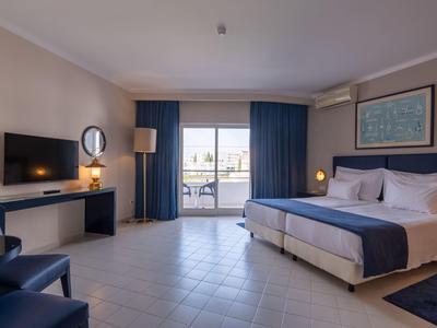 Modernes Hotelzimmer mit Doppelbett, blauem und weißem Farbkonzept, Balkon und Schreibtisch.