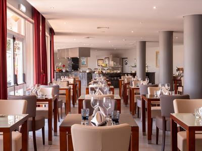 Helles Restaurant mit vielen Holztischen, weißen Stühlen und eingedeckten Tischen mit Gläsern.