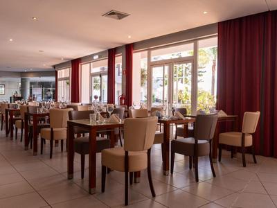 Ein heller, moderner Speisesaal mit vielen Holztischen und gepolsterten Stühlen neben großen Fenstern.