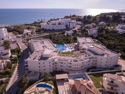 Große weiße Hotelanlage mit Pool an der Küste, umgeben von Grünflächen und weiteren Gebäuden.