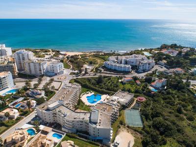Luftaufnahme einer Küstenstadt mit Hotels, Pools, Tennisplätzen und blauem Meer im Hintergrund.