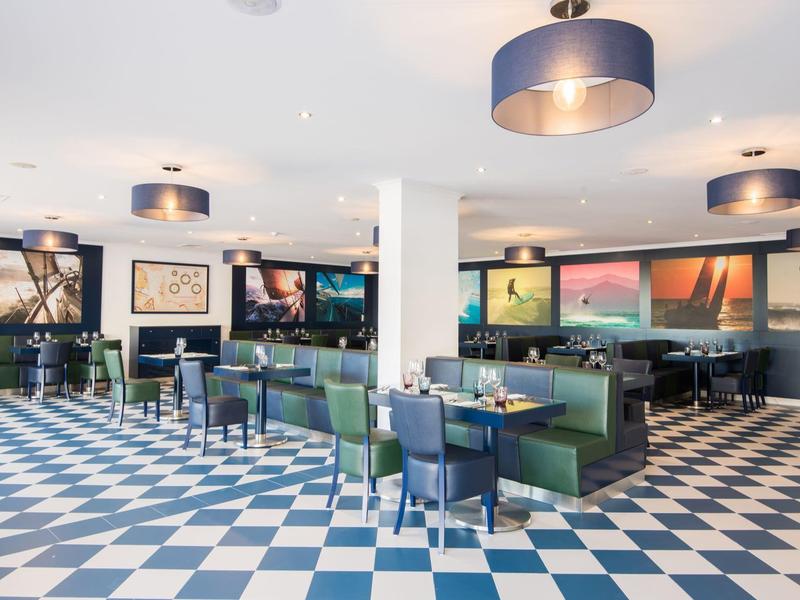 Moderner Speiseraum mit blau-weiß kariertem Boden, grünen Sitzbänken und runden Lampen an der Decke.