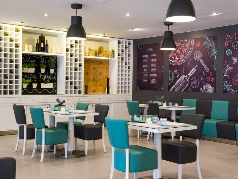 Modernes Café mit weißen Tischen, türkisfarbenen Stühlen und dunklen Wandkarten.