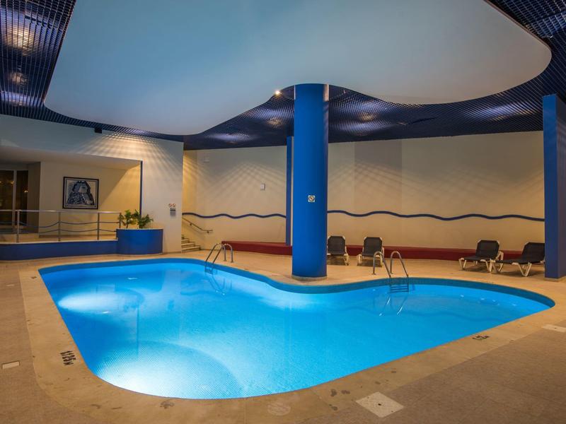 Innenpool mit geschwungener Form, blauer Beleuchtung, Säulen und Sitzbereich an der Wand.