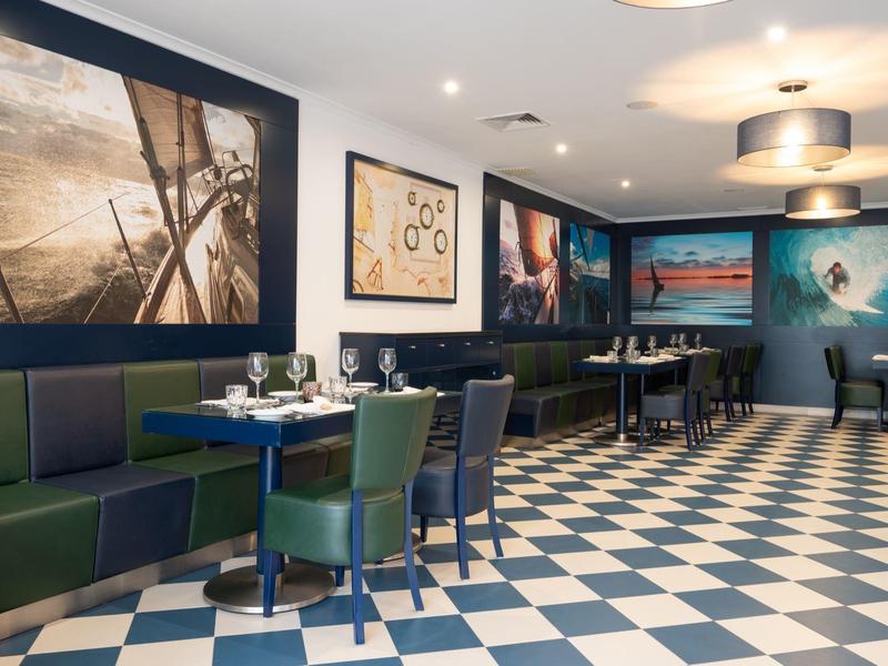 Restaurant mit blau-grünen Stühlen, dunkelblauen Wänden, großen Gemälden und kariertem Fliesenboden.