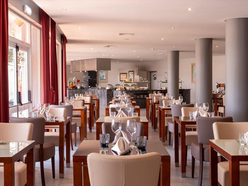 Helles Restaurant mit vielen Holztischen, weißen Stühlen und eingedeckten Tischen mit Gläsern.