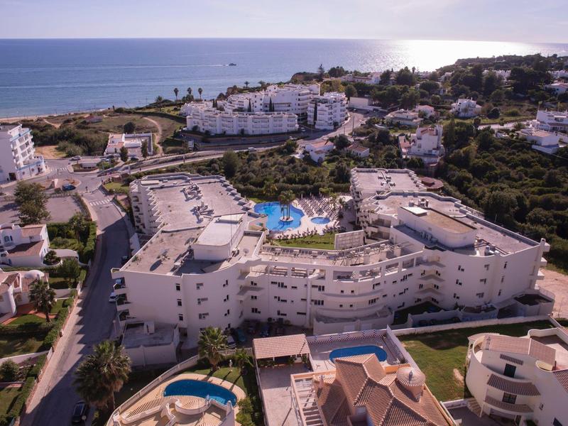 Große weiße Hotelanlage mit Pool an der Küste, umgeben von Grünflächen und weiteren Gebäuden.