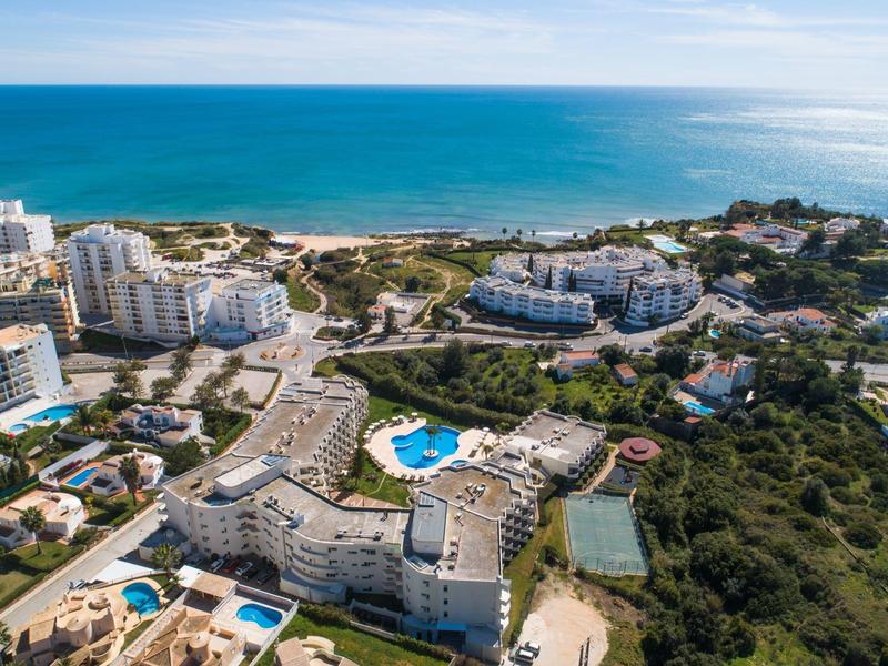 Luftaufnahme einer Küstenstadt mit Hotels, Pools, Tennisplätzen und blauem Meer im Hintergrund.