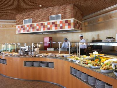 Buffet mit vielfältigen Speisen auf gebogenem Holztresen in hellem, modernem Restaurant.