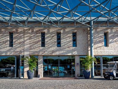 Modernes Gebäude mit großen Fenstern, steinerner Fassade und blauem Glasdach.