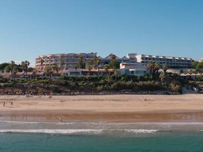 Strand mit Sand, darüber Hotels auf grünen Felsen unter klarem blauem Himmel.