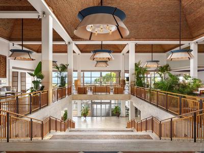 Großer heller Raum mit Holzbalken, grünen Pflanzen und modernen Lampen in einem Eingangsbereich.