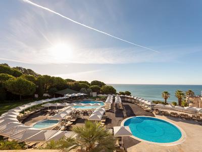 Luxuriöse Poolanlage mit zwei großen Pools, Liegestühlen und Meerblick unter klarem Himmel.