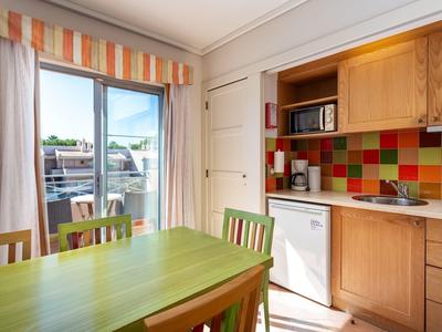 Helle Küche mit buntem Fliesenspiegel, grünem Tisch und Holzschränken, Balkon mit Sonnenschutz.