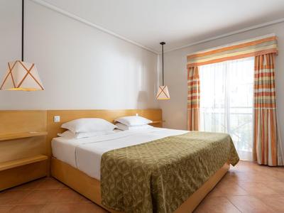 Helles Schlafzimmer mit zwei Einzelbetten, Holzmöbeln, beigem Bettüberwurf und karierten Vorhängen.