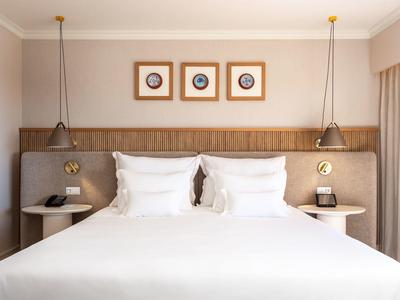 Ein großes Doppelbett mit weißen Kissen, zwei hängenden Lampen und drei gerahmten Bildern an der Wand.