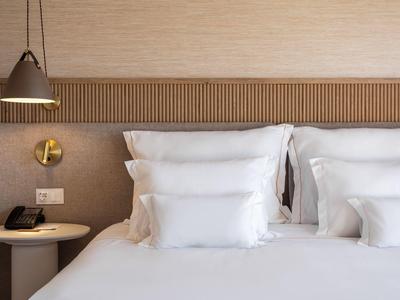 Modernes Schlafzimmer mit weißen Kissen, Holzverkleidung, Nachttisch, Telefon und hängender Lampe.