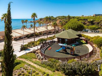 Park mit Rundbühne, Palmen und Blick auf das blaue Meer im Hintergrund bei Sonnenschein.
