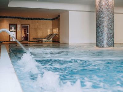 Moderner Innenpool mit Sprudelwasser, hellem Mosaikpfeiler und entspannenden Lounge-Bereichen.